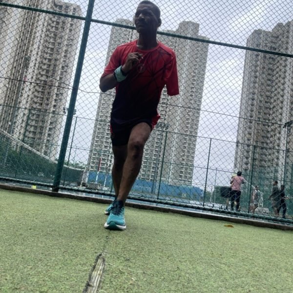 Athlete sprinting hard on the track with the Lodha Amara towers behind — VHR Sports