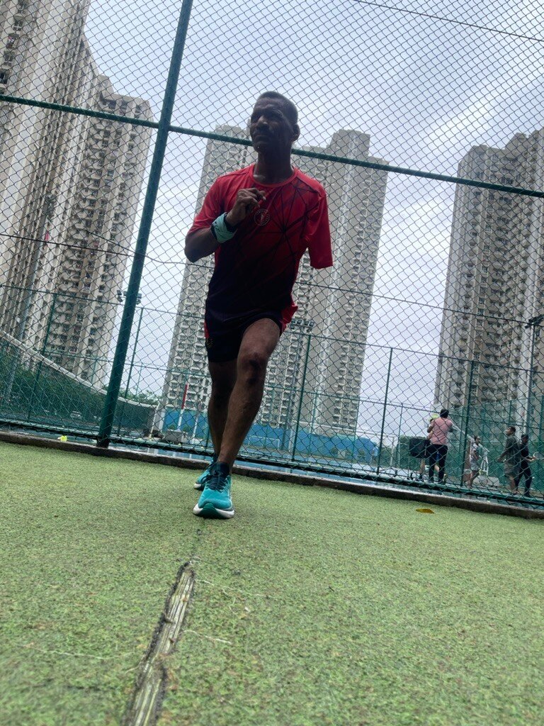 Athlete sprinting hard on the track with the Lodha Amara towers behind — VHR Sports